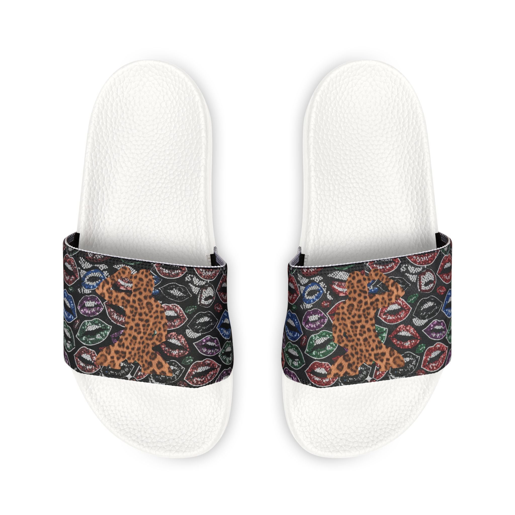 A pair of white slide sandals with wide straps featuring a busy pattern of leopard print, colorful lips, and small circular motifs on a black background.