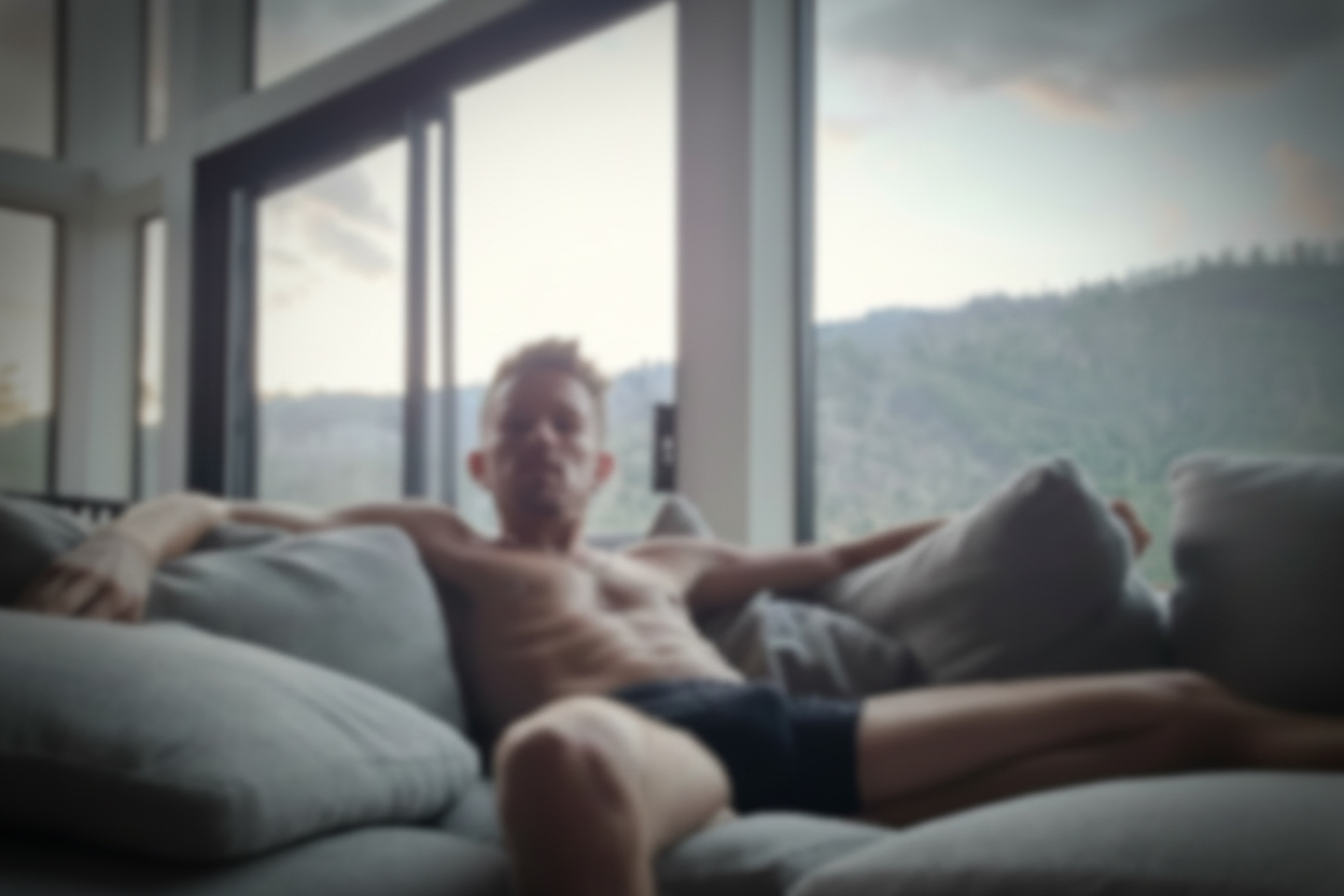 Man sitting on a couch with a reflective surface showing his reflection.
